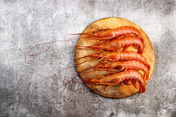Argentinian raw red prawns (shrimps) with heads on a round wooden cutting board on a dark grey background. Top view, flat lay