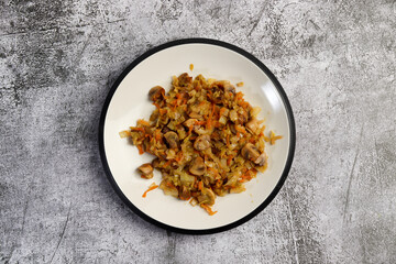 Stewed cabbage with champignon mushrooms on a round plate on a dark gray background. Top view, flat lay
