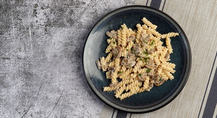 Creamy pasta with champignon mushrooms on a round plate on a dark gray background. Top view, flat lay