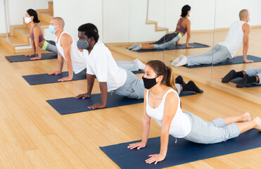 Fototapeta na wymiar People in protective masks practice yoga in the gym