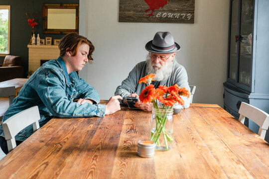 Grandfather checking his grandson's cell phone at home