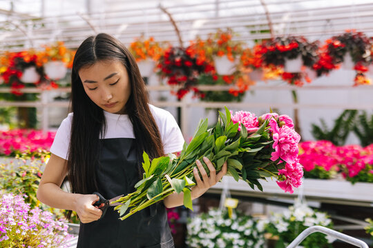 Female worker trimming stem in bunch of pink flowers 