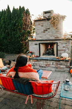 woman sits in front of outdoor fireplace in early fall