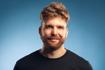 Fototapeta premium Male beauty concept. Emotive portrait of cute charismatic active 30-year-old man posing over blue background. Perfect haircut. Hipster style. Close up. Text space. Studio head shot