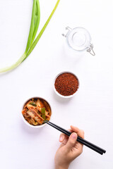 Hand holding chopsticks and eating kimchi cabbage on white background, Korean homemade fermented side dish food, Top view