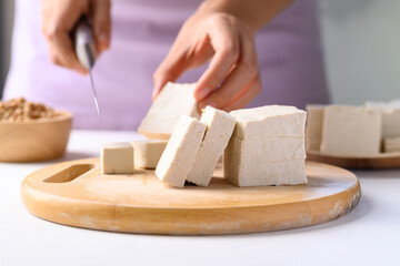 Hand holding knife and cutting organic tofu on wooden board prepare for cooking, Vegan food ingredients in Asian cuisine, plant based