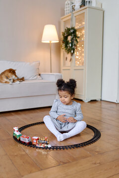 a little girl near the Christmas tree plays a toy train