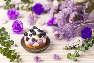 Obraz na płótnie Canvas Blueberry Graham Cheesecake topped with fresh berries on white drift wood vintage table over a dry flowers and twigs background.