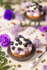 White chocolate and blueberry sable tartelette with vintage spoon on a white drift wood table with purple dry flowers background. Vertical view.