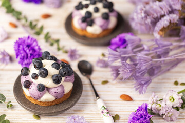 Obraz na płótnie Canvas White chocolate and blueberry sable tartelette with vintage spoon on a white drift wood table with purple dry flowers background.