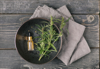 Glass bottle with CBD oil, THC tincture and hemp leafson a black plate on a wooden background....