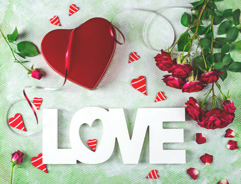 Festive composition of love for Valentines day made with red gift box and roses, hearts and word Love. Flat lay.