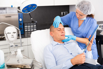 Skilled woman beautician consulting male client before facial treatment in medical esthetic office