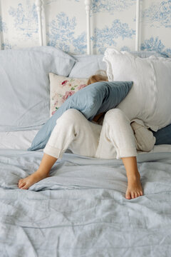 The girl hid in the pillows on the bed.