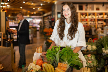 Portrait of a smiling young girl with a full grocery cart, who came to the suprmarket to make...