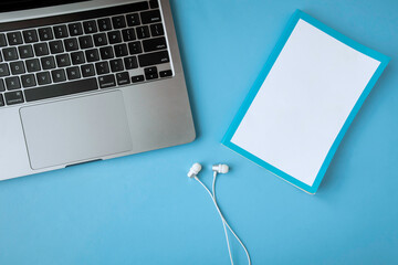 Headphone, white book and laptop keyboard on blue background.