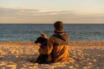 man and dog sitting at beach on sunset