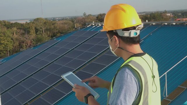 A young Asian engineer is checking with a tablet the sun's operation and cleanliness on the field of photovoltaic solar panels at sunset.