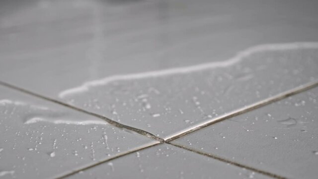 Clean water flows on floor covering white ceramic tile because of hard pipe damage causing flood in apartment bathroom close view.