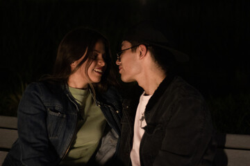 young engaged couple look at each other and smile, they have a date in the park at night.
