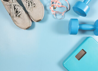 flat lay of blue weight scale, blue dumbbells, gray sneakers and measuring tape on blue background with copy space. Sports and weight loss concept.