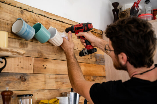 Man drilling hole to hang coffe mugs on wooden wall 