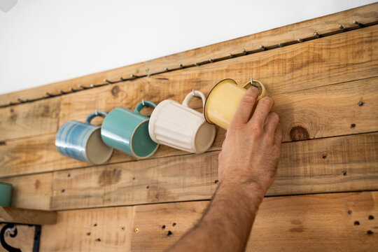 Detail of Man hanging coffe mugs on wooden wall 