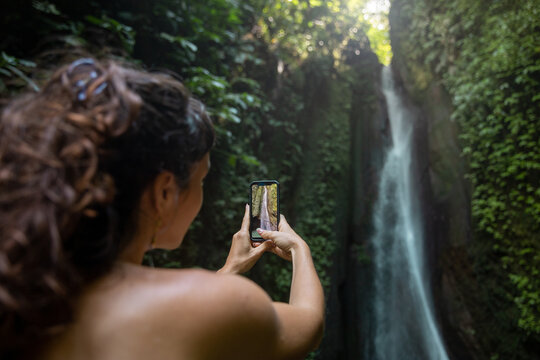 Woman taking picture of waterfall on smartphone