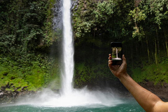 Woman holding Cell phone taking picture lush waterfall 