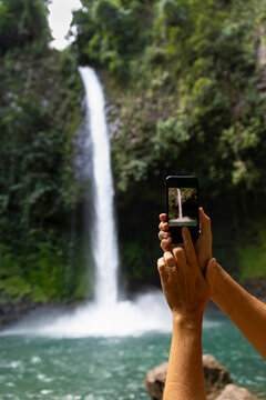 Hand holding Cell phone taking picture of waterfall 