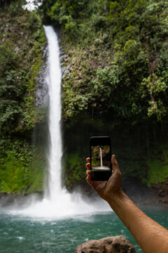 Woman holding Cell phone taking picture of waterfall 
