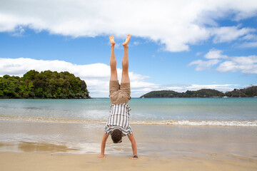 A traveler performs a handstand in the golden sand of Bathing Beach, Oban, Stewart Island, New...
