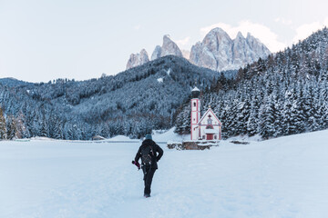 woman walks through the snow to church in the middle of the alps with snow-capped mountains in the...
