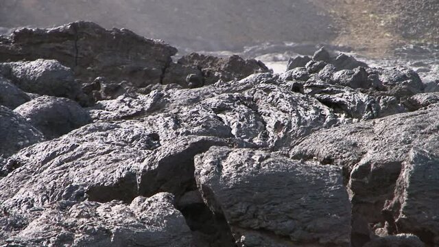 detail of solidified lava with some steam rising, slope of a hill in background