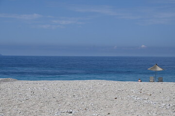 Strand mit Meer und Sonnenschirm an der Küste in Albanien, mit blauem Himmel 