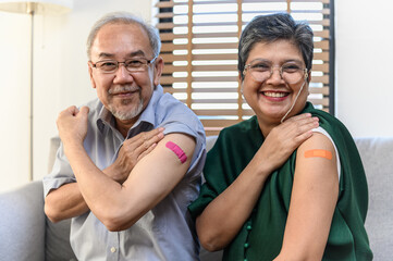 Healthy Asian senior couple showing bandage plaster on arm after received covid vaccination for prevent covid-19 infection. Coronavirus pandemic protection health care senior lifestyle concept.