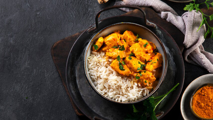 Indian butter chicken curry with basmati rice on dark background.