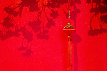 Hanging pendant for Chinese new year ornament with shadow of peach blossom flowers on red glitter paper background.