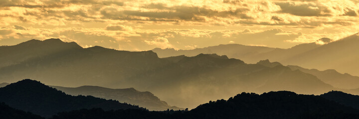panoramic of the silhouette of the mountains at sunset with a cloudy sky.
