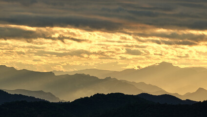 silhouette of mountains at sunset with a cloudy sky.