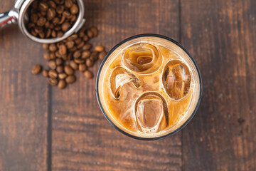 A cup of Iced Latte Coffee with ice cubes placed on a wooden table in a coffee shop