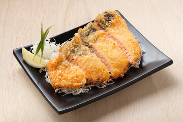 Japanese food, Tonkatsu salmon fish deep fried with bread crumbs cutlet in black plate on wooden background.