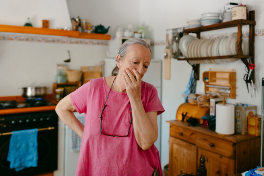 Elderly woman in pink thinking in the kitchen