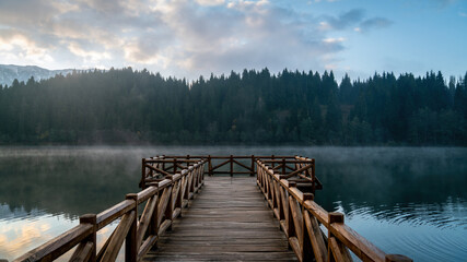 Fototapeta premium Wooden pier in Savsat Karagol Black lake in Eastern Black Sea region with morning evaporation. Savsat Karagol lake is a large trout lake in the forest in Artvin, Turkey