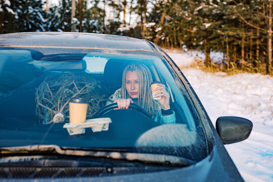 Woman drinking coffee in a car bringing Christmas tree