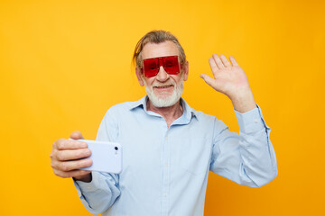Naklejka premium Senior grey-haired man in fashionable red glasses with a phone isolated background
