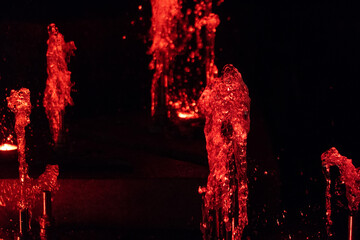 Colorful water in the singing fountain. Red light splashes closeup during the beautiful fountain show at night.