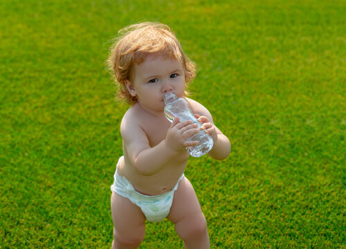 Baby Child Drinking Water. Child Resting In Grass Park On Nature. Kids Drinks Clean Water In Summer.