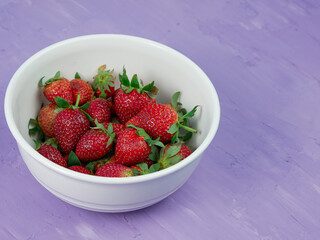 Strawberries in a white bowl on a purple background. healthy and vegetarian fruit concept
