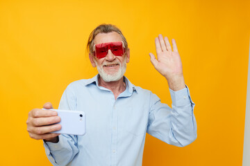 Naklejka premium old man in fashionable red glasses with a phone yellow background